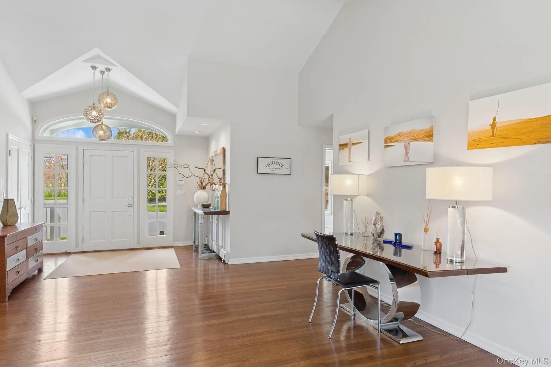 Foyer entrance featuring a notable chandelier, high vaulted ceiling, wood finished floors, and baseboards Foyer entrance featuring a notable chandelier, high vaulted ceiling, wood finished floors, and baseboards