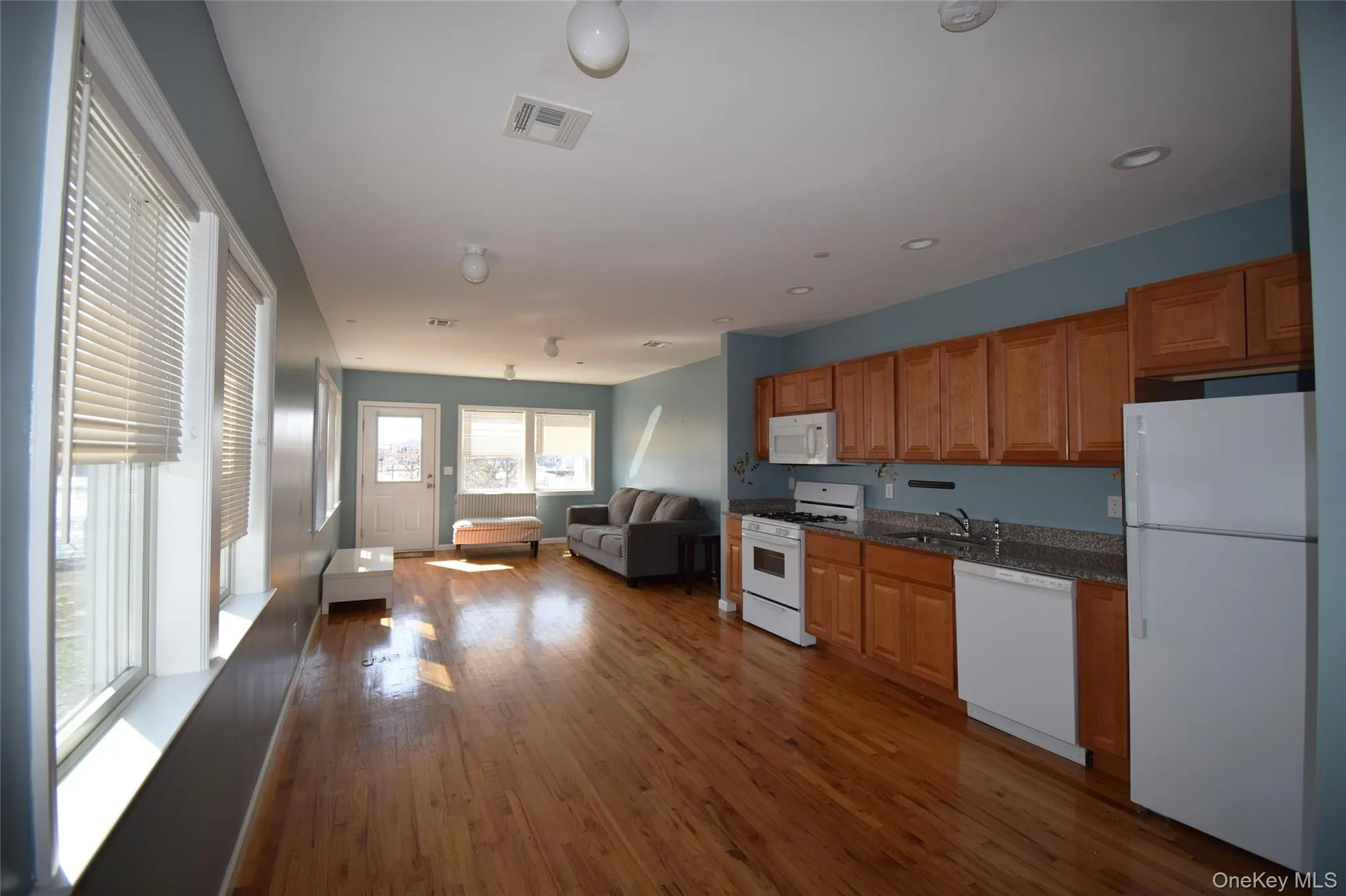 Open kitchen and living room concept with dark wood-style floors, visible vents, a sink, and white appliances Open kitchen and living room concept with dark wood-style floors, visible vents, a sink, and white appliances