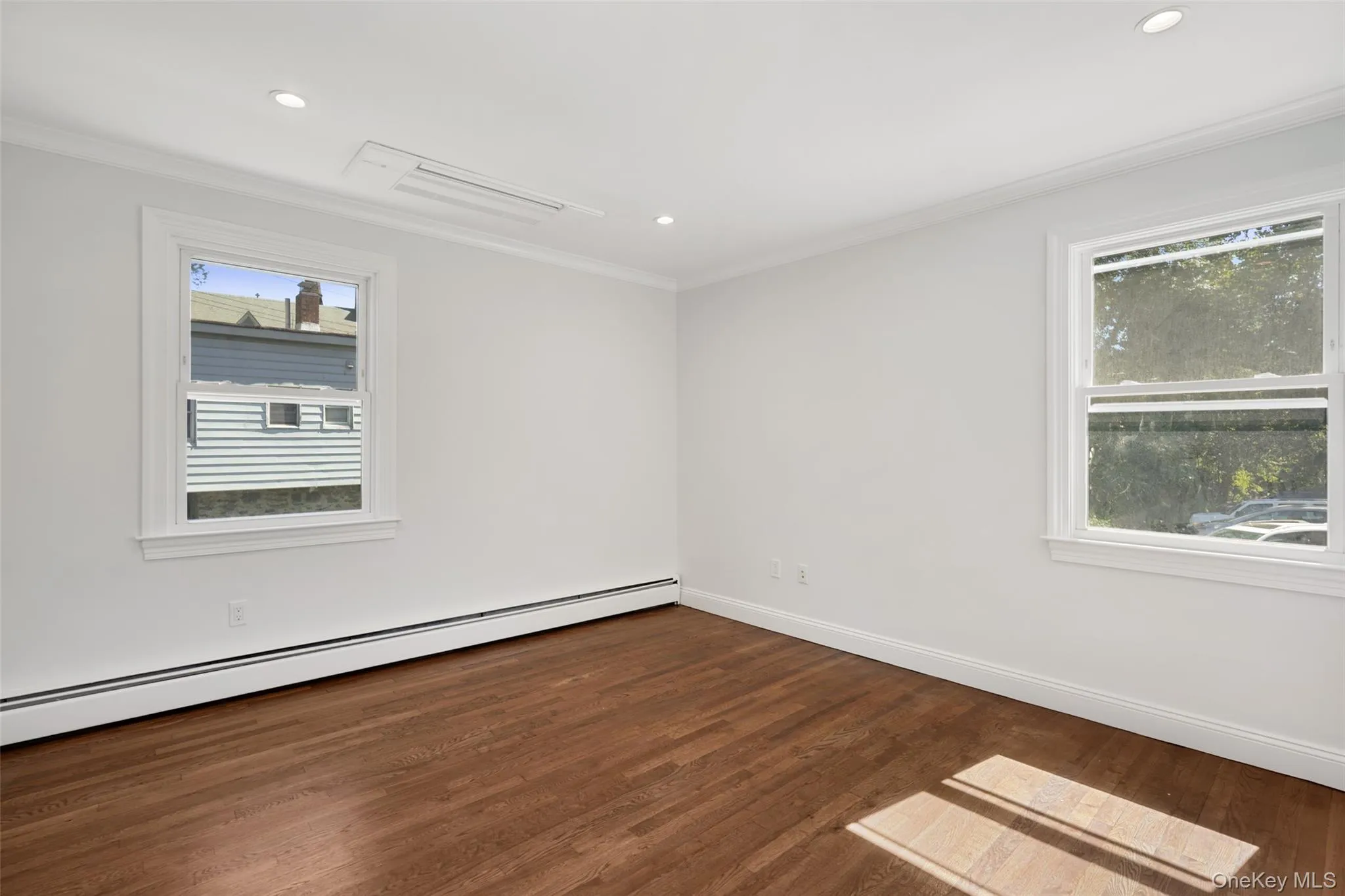 Spare room with a baseboard heating unit, ornamental molding, dark wood-style flooring, plenty of natural light, and recessed lighting Spare room with a baseboard heating unit, ornamental molding, dark wood-style flooring, plenty of natural light, and recessed lighting