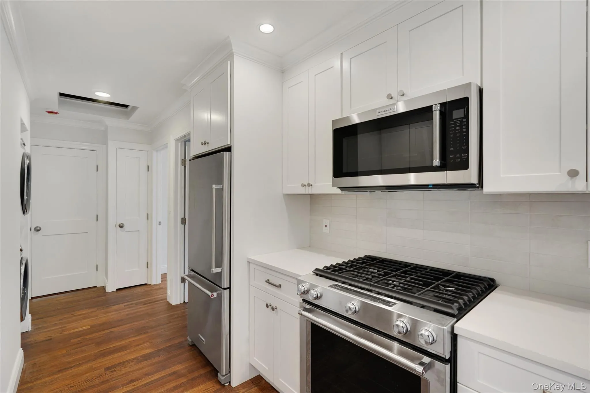 Kitchen with stainless steel appliances, ornamental molding, white cabinetry, backsplash, and dark wood-style flooring Kitchen with stainless steel appliances, ornamental molding, white cabinetry, backsplash, and dark wood-style flooring