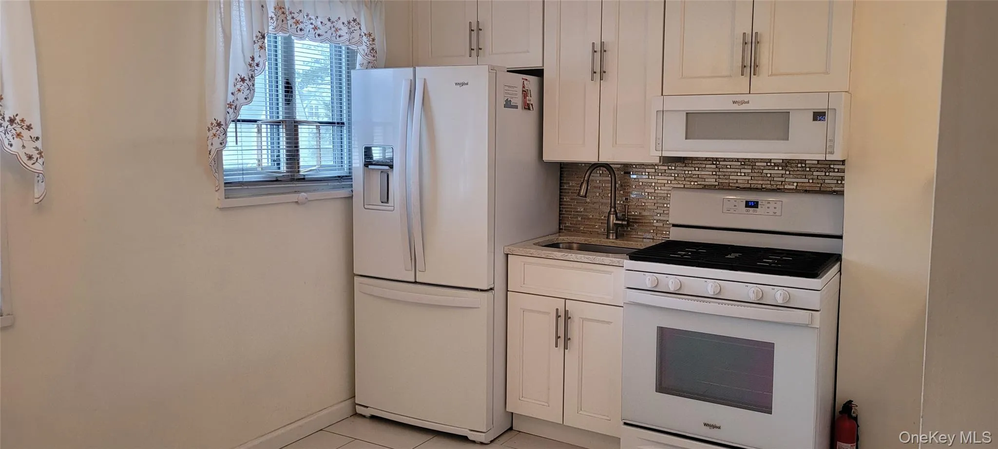 Kitchen with tasteful backsplash, a sink, white appliances, light tile patterned floors, and white cabinets Kitchen with tasteful backsplash, a sink, white appliances, light tile patterned floors, and white cabinets