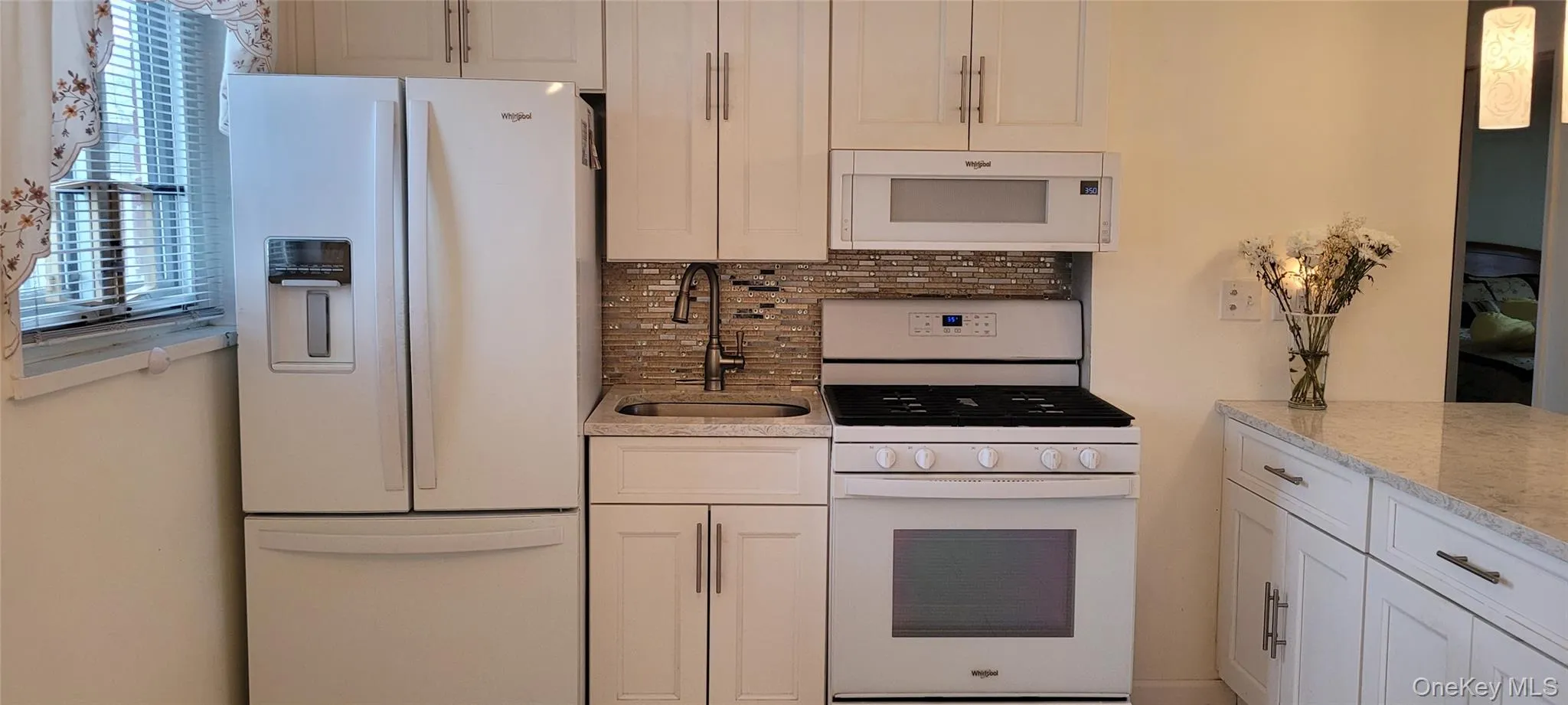 Kitchen featuring decorative backsplash, white cabinetry, a sink, and white appliances Kitchen featuring decorative backsplash, white cabinetry, a sink, and white appliances