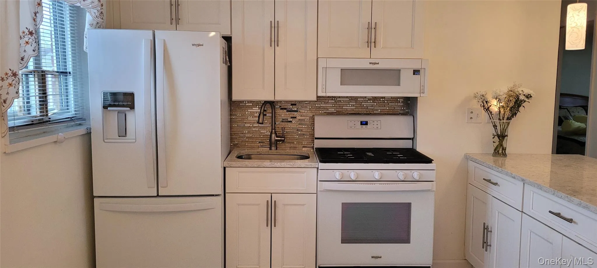 Kitchen with white cabinets, a sink, tasteful backsplash, white appliances, and light stone countertops Kitchen with white cabinets, a sink, tasteful backsplash, white appliances, and light stone countertops
