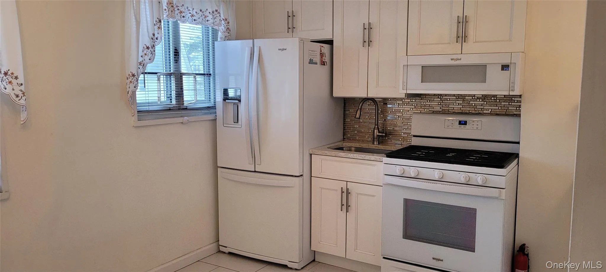 Kitchen with a sink, white cabinetry, decorative backsplash, white appliances, and light tile patterned floors Kitchen with a sink, white cabinetry, decorative backsplash, white appliances, and light tile patterned floors