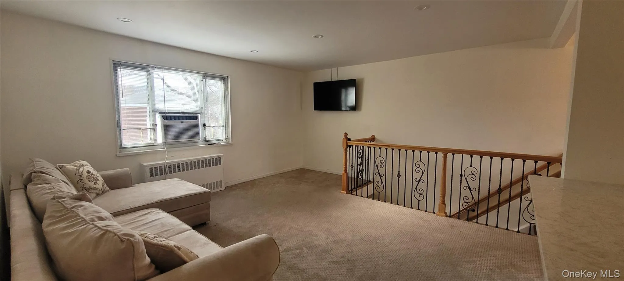 Living area with radiator, cooling unit, baseboards, an upstairs landing, and carpet floors Living area with radiator, cooling unit, baseboards, an upstairs landing, and carpet floors