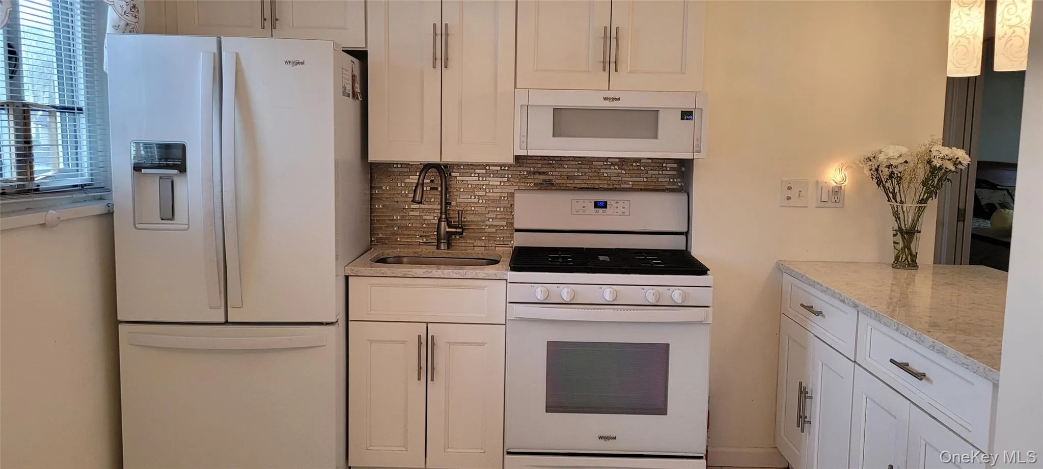 Kitchen featuring light stone counters, tasteful backsplash, a sink, white appliances, and white cabinetry Kitchen featuring light stone counters, tasteful backsplash, a sink, white appliances, and white cabinetry