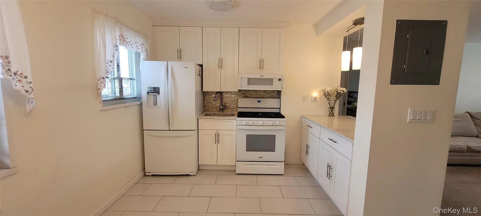 Kitchen featuring electric panel, a sink, backsplash, white cabinetry, and white appliances Kitchen featuring electric panel, a sink, backsplash, white cabinetry, and white appliances