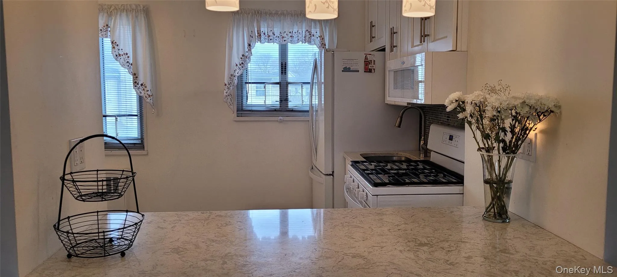 Kitchen with decorative light fixtures, white cabinetry, and white appliances Kitchen with decorative light fixtures, white cabinetry, and white appliances