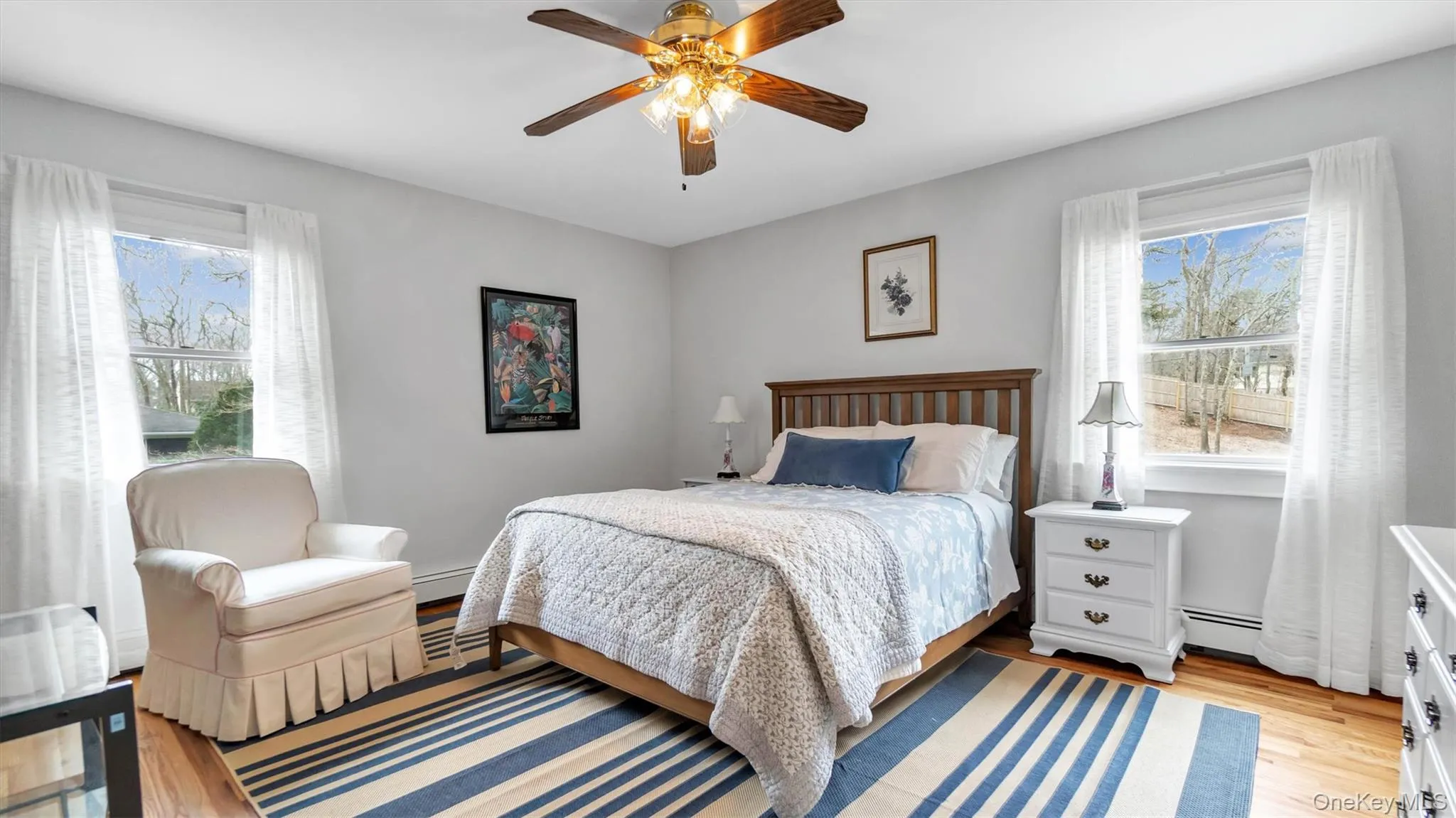 Bedroom featuring a baseboard radiator, multiple windows, ceiling fan, and light wood-style floors Bedroom featuring a baseboard radiator, multiple windows, ceiling fan, and light wood-style floors
