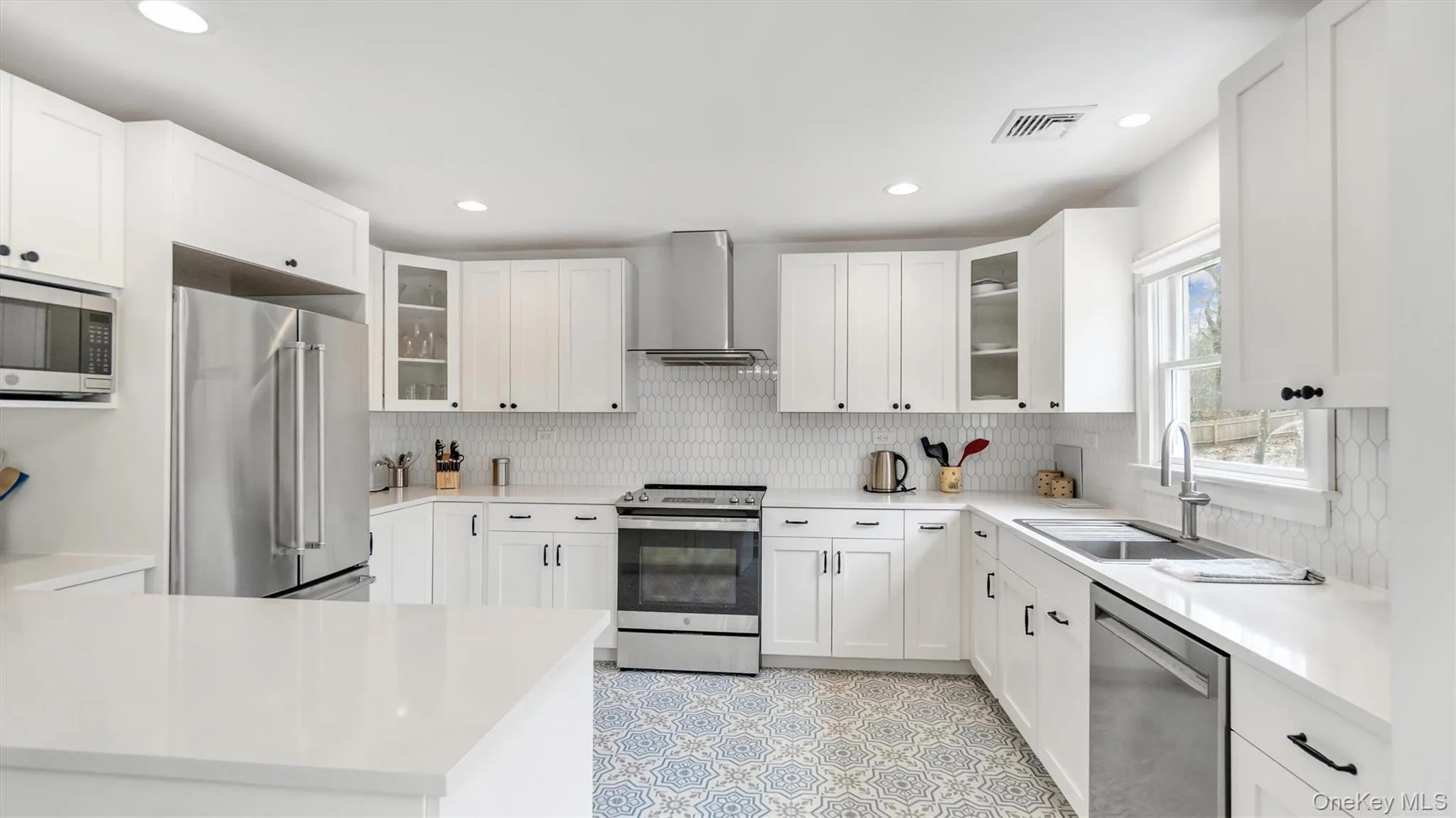 Kitchen with wall chimney range hood, a sink, stainless steel appliances, backsplash, and visible vents Kitchen with wall chimney range hood, a sink, stainless steel appliances, backsplash, and visible vents