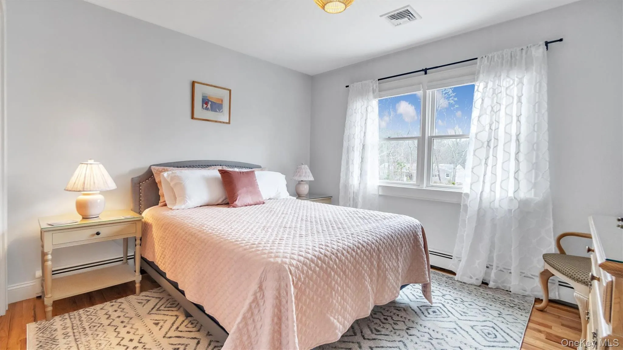 Bedroom featuring a baseboard heating unit, baseboards, wood finished floors, and visible vents Bedroom featuring a baseboard heating unit, baseboards, wood finished floors, and visible vents