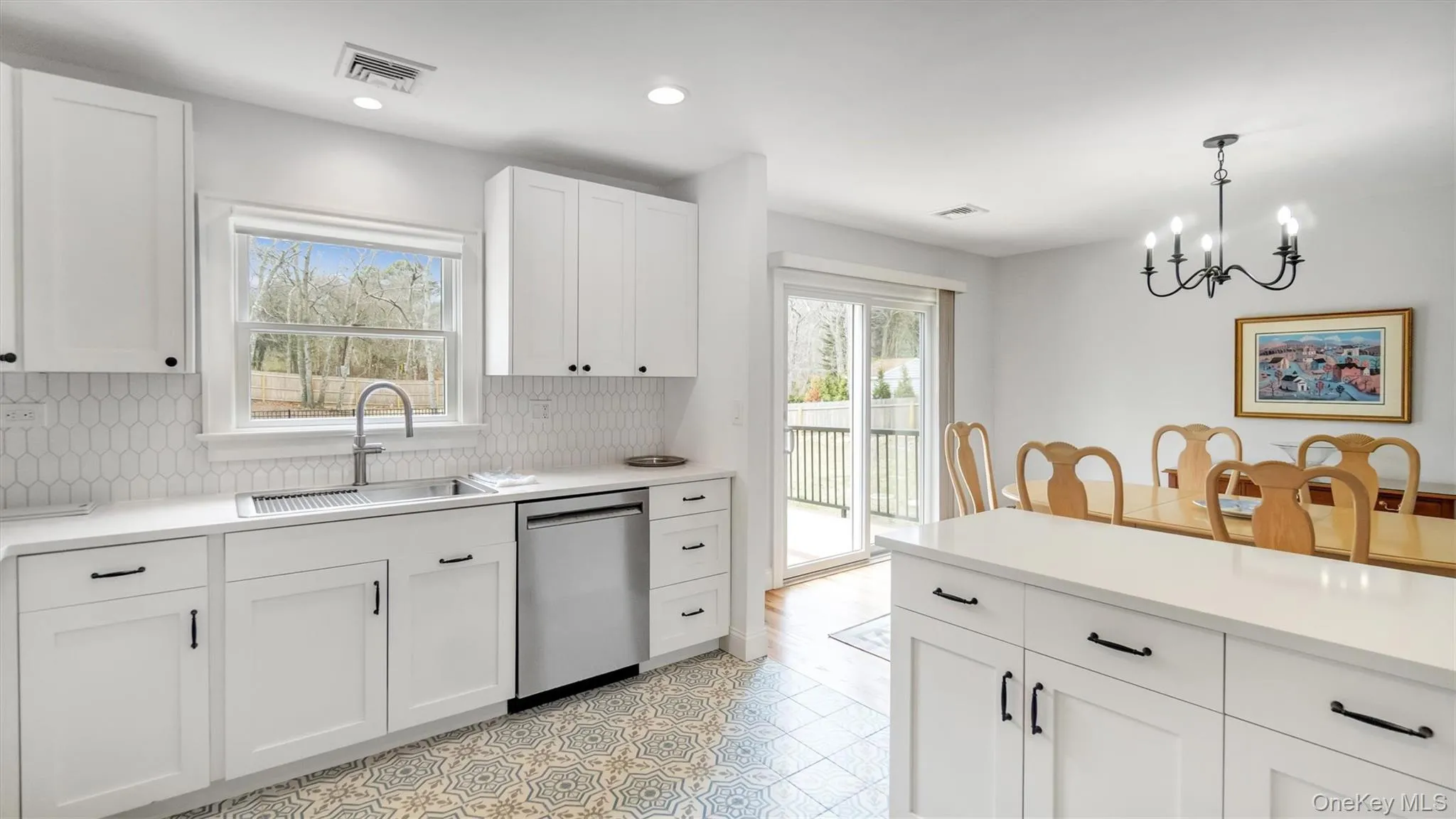 Kitchen with stainless steel dishwasher, tasteful backsplash, a sink, a chandelier, and white cabinetry Kitchen with stainless steel dishwasher, tasteful backsplash, a sink, a chandelier, and white cabinetry