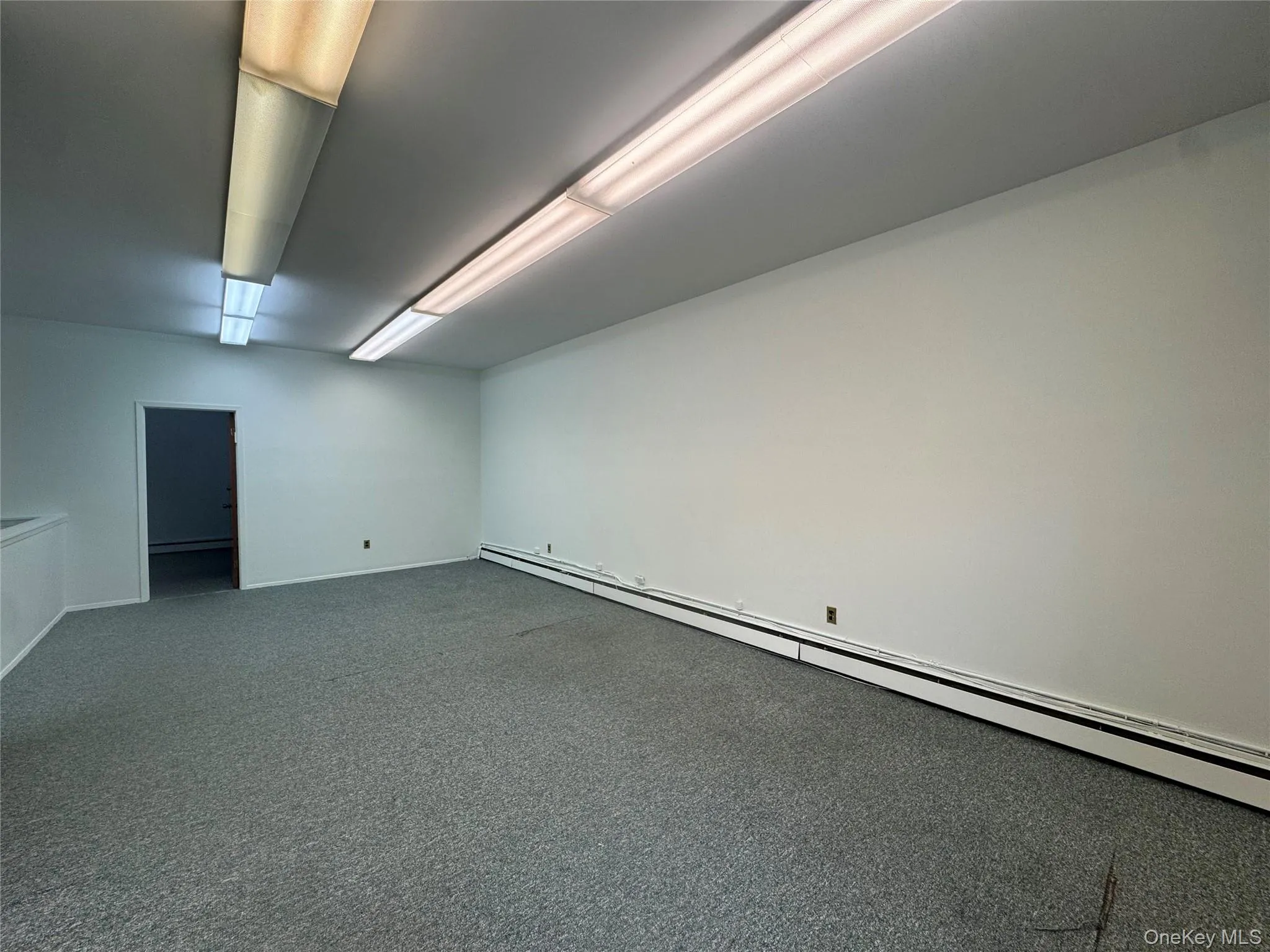 Empty room with a baseboard heating unit, a baseboard radiator, dark colored carpet, and baseboards Empty room with a baseboard heating unit, a baseboard radiator, dark colored carpet, and baseboards