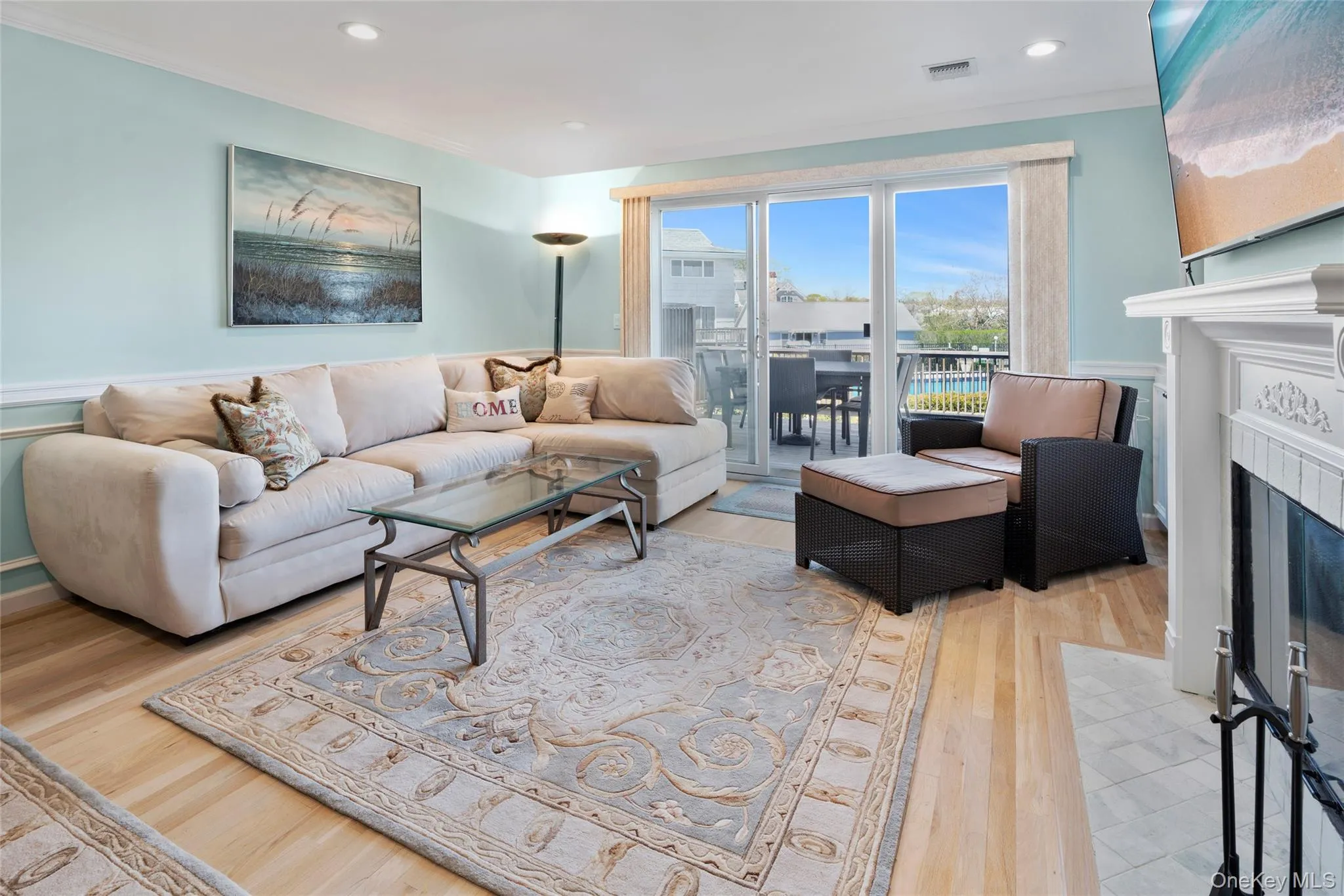 Living area with a fireplace with flush hearth, recessed lighting, wood finished floors, visible vents, and crown molding Living area with a fireplace with flush hearth, recessed lighting, wood finished floors, visible vents, and crown molding