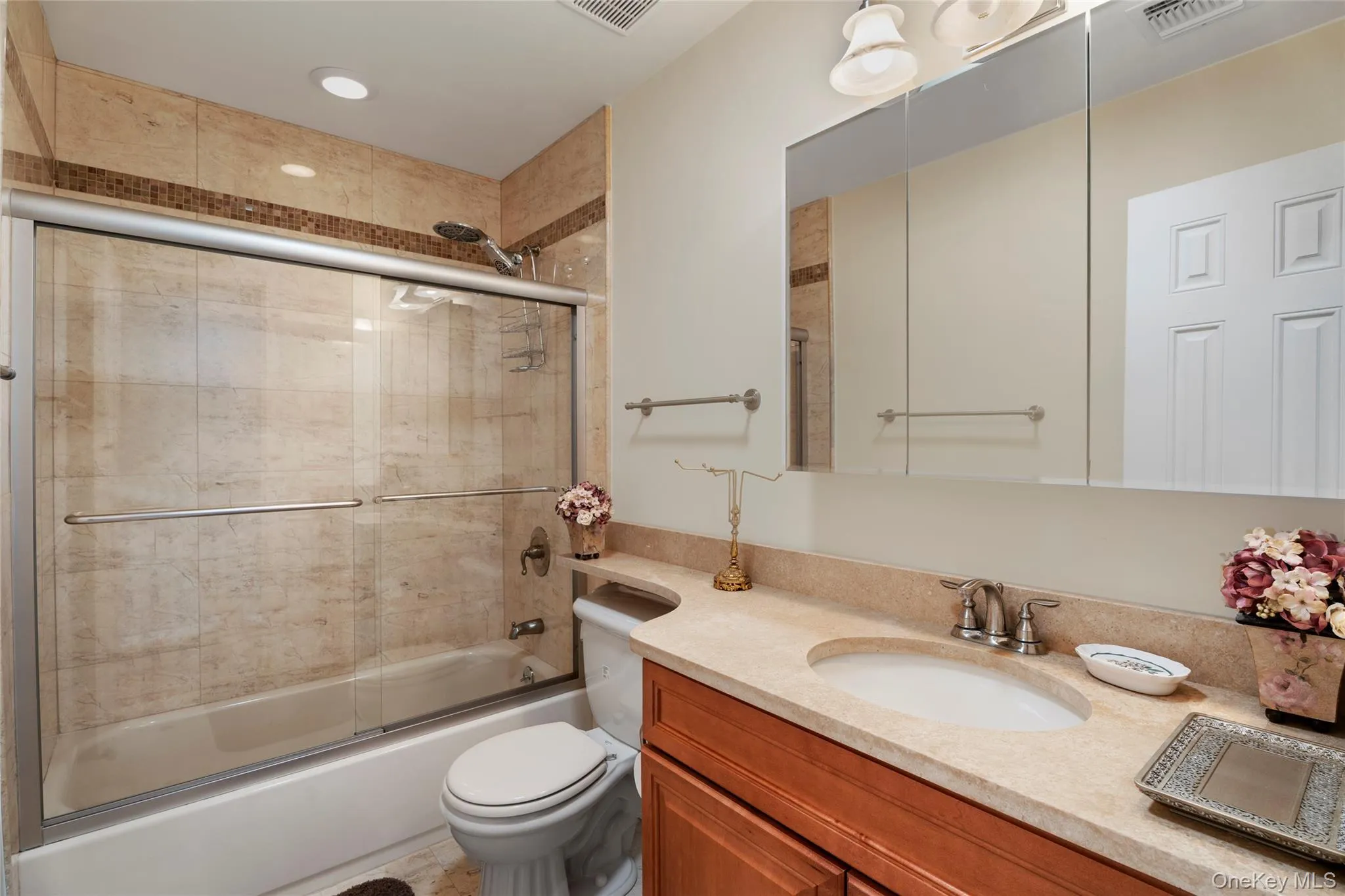 Full bathroom featuring enclosed tub / shower combo, toilet, vanity, and visible vents Full bathroom featuring enclosed tub / shower combo, toilet, vanity, and visible vents