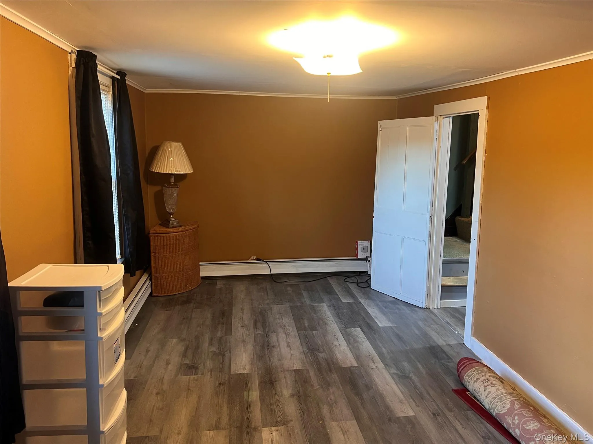 Unfurnished bedroom featuring ornamental molding, dark wood-style floors, baseboard heating, and a baseboard radiator Unfurnished bedroom featuring ornamental molding, dark wood-style floors, baseboard heating, and a baseboard radiator