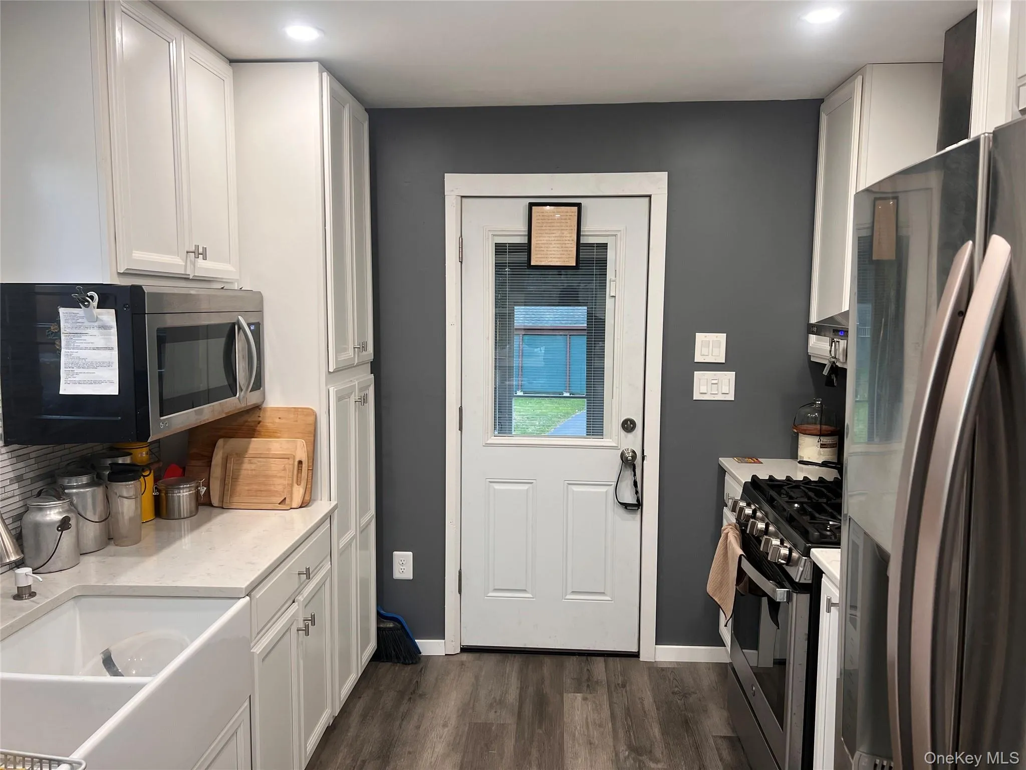 Kitchen featuring stainless steel appliances, white cabinetry, dark wood finished floors, recessed lighting, and backsplash Kitchen featuring stainless steel appliances, white cabinetry, dark wood finished floors, recessed lighting, and backsplash