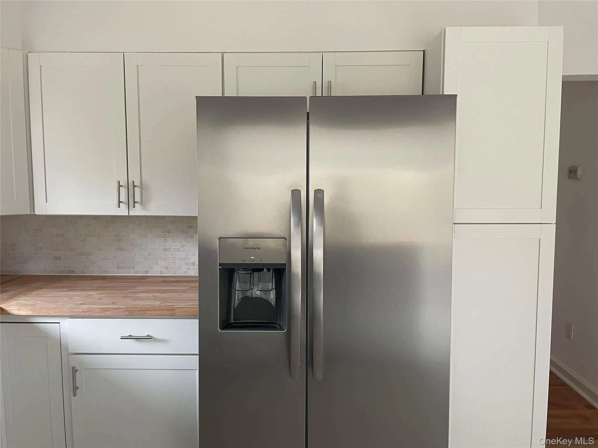 Kitchen featuring stainless steel fridge with ice dispenser, white cabinets, butcher block counters, and tasteful backsplash Kitchen featuring stainless steel fridge with ice dispenser, white cabinets, butcher block counters, and tasteful backsplash