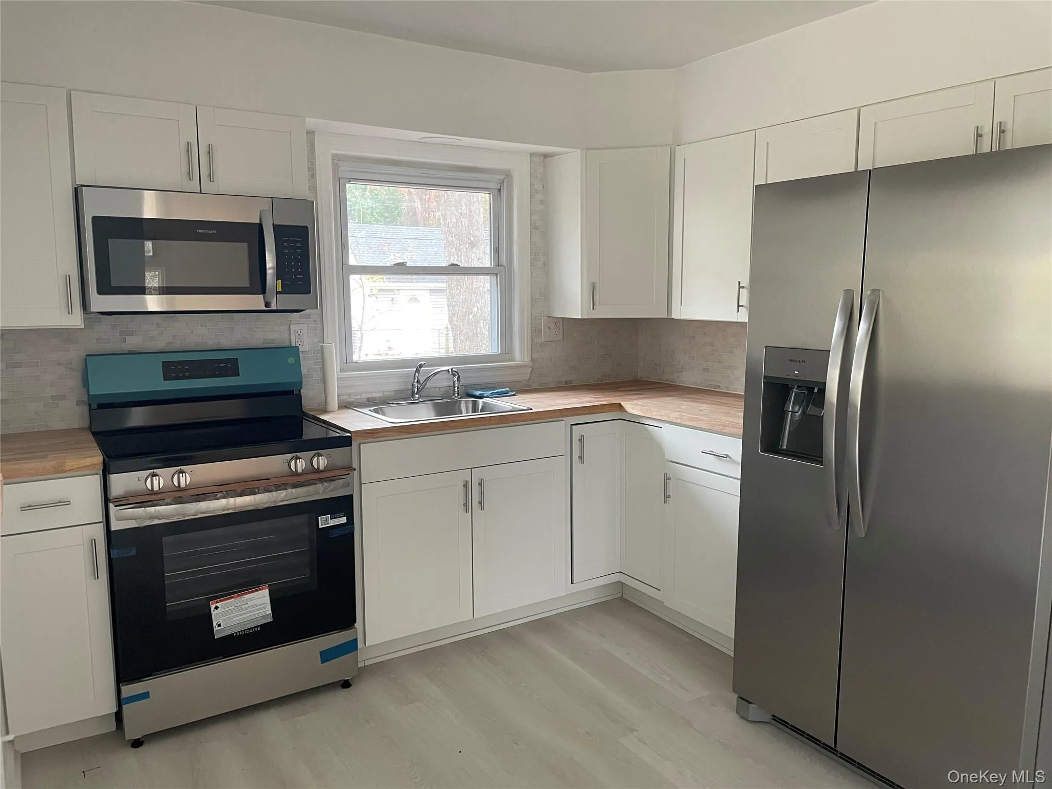 Kitchen featuring stainless steel appliances, white cabinets, light wood-style flooring, and decorative backsplash Kitchen featuring stainless steel appliances, white cabinets, light wood-style flooring, and decorative backsplash