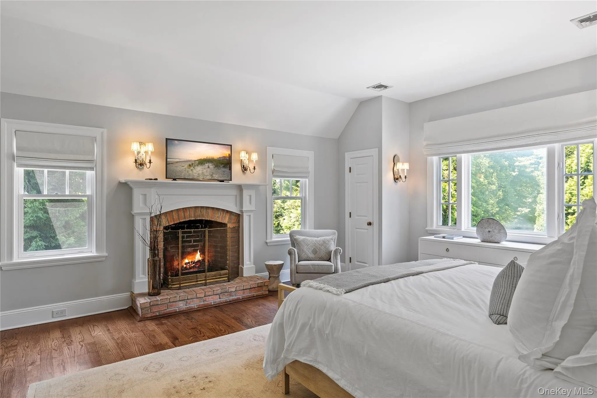 Bedroom with multiple windows, wood finished floors, visible vents, and a brick fireplace Bedroom with multiple windows, wood finished floors, visible vents, and a brick fireplace