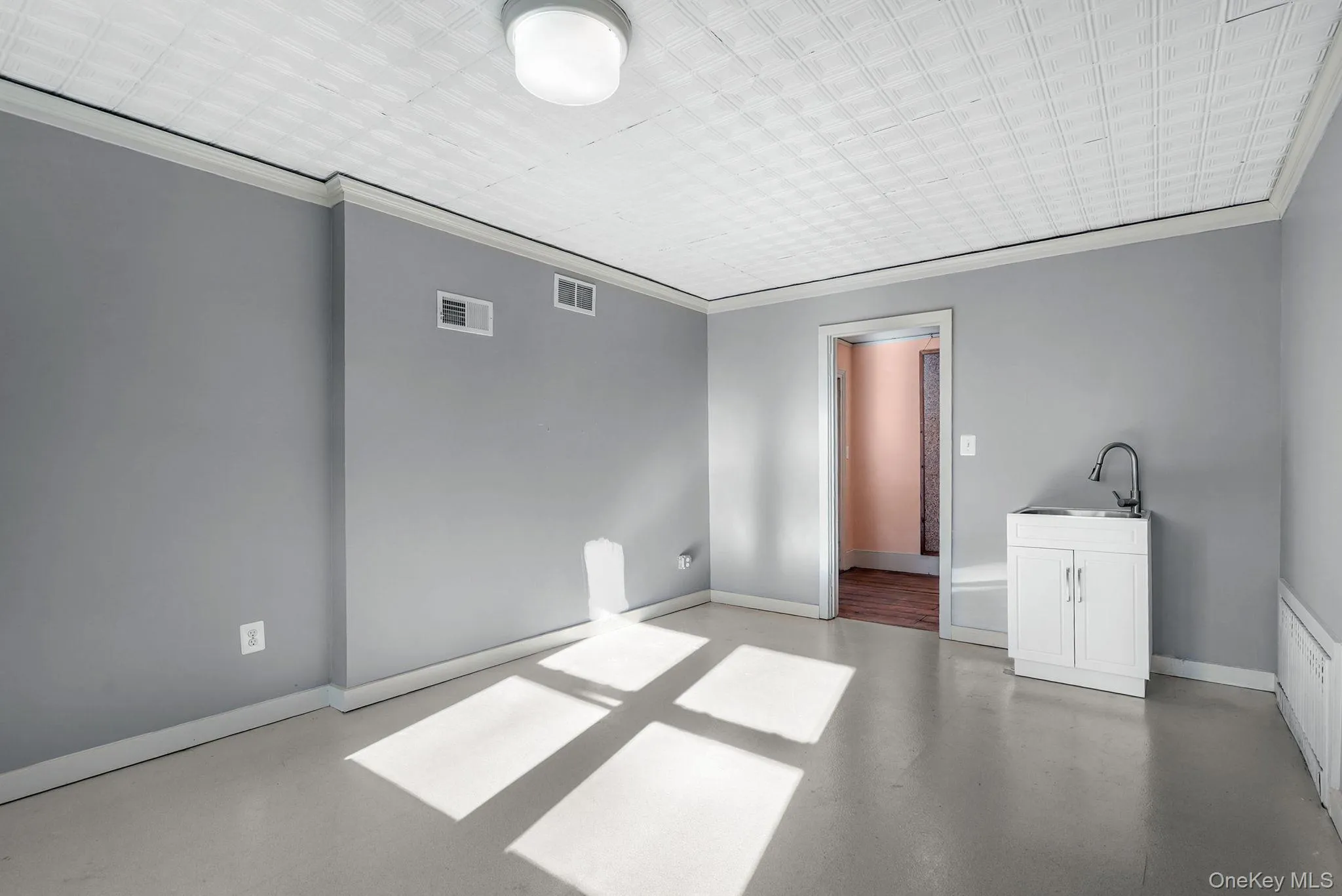 Empty room featuring baseboards, visible vents, a sink, and concrete floors Empty room featuring baseboards, visible vents, a sink, and concrete floors