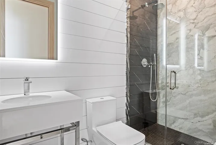 Bathroom with toilet, vanity, and a marble finish shower