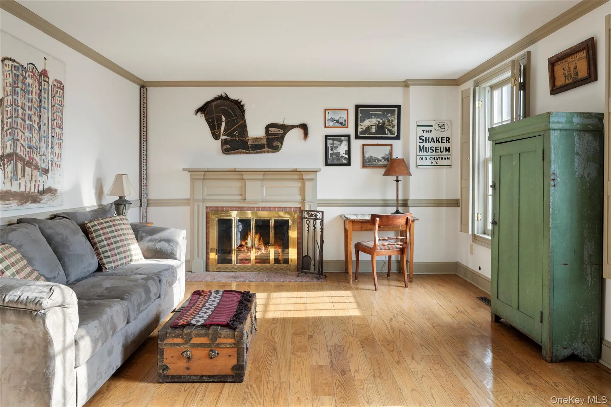 Living area featuring wood finished floors, a brick fireplace, crown molding, and baseboards Living area featuring wood finished floors, a brick fireplace, crown molding, and baseboards