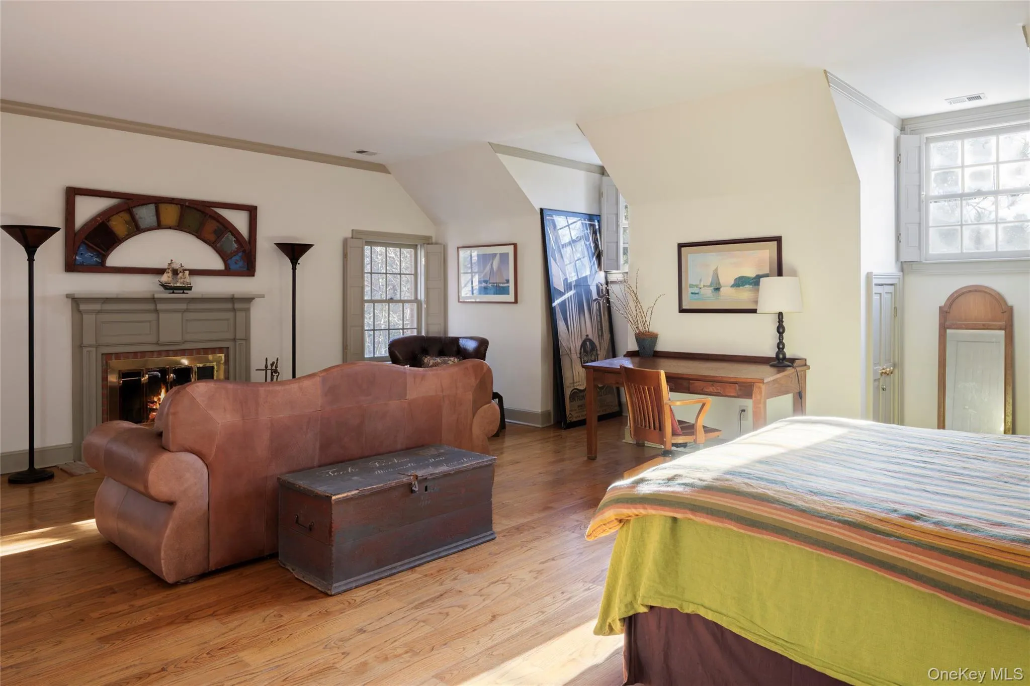 Bedroom featuring light wood-style flooring, visible vents, a lit fireplace, and multiple windows Bedroom featuring light wood-style flooring, visible vents, a lit fireplace, and multiple windows