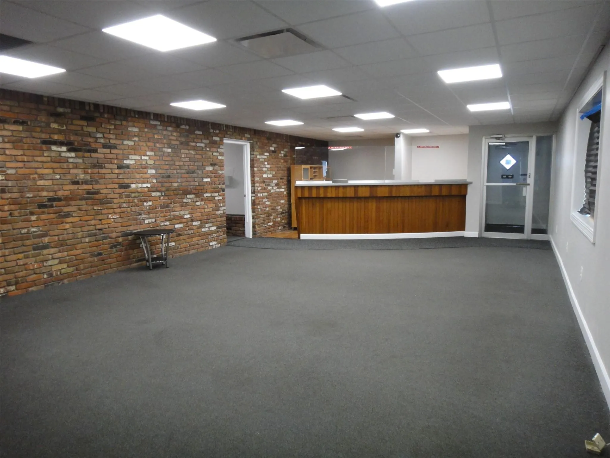 Empty room with a drop ceiling, a bar, brick wall, baseboards, and dark carpet Empty room with a drop ceiling, a bar, brick wall, baseboards, and dark carpet