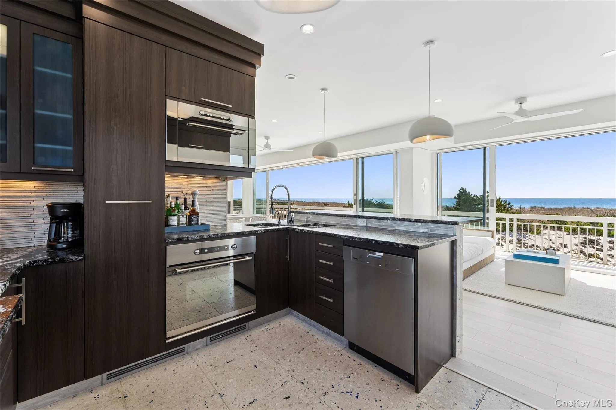 Kitchen featuring dark stone counters, a sink, appliances with stainless steel finishes, dark brown cabinets, and a peninsula Kitchen featuring dark stone counters, a sink, appliances with stainless steel finishes, dark brown cabinets, and a peninsula