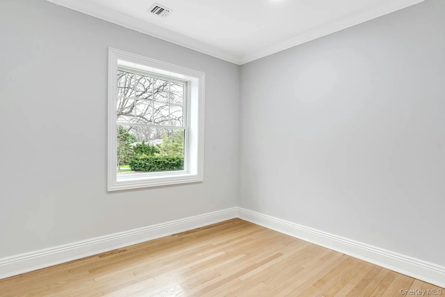 Spare room with light wood-style floors, baseboards, crown molding, and visible vents Spare room with light wood-style floors, baseboards, crown molding, and visible vents