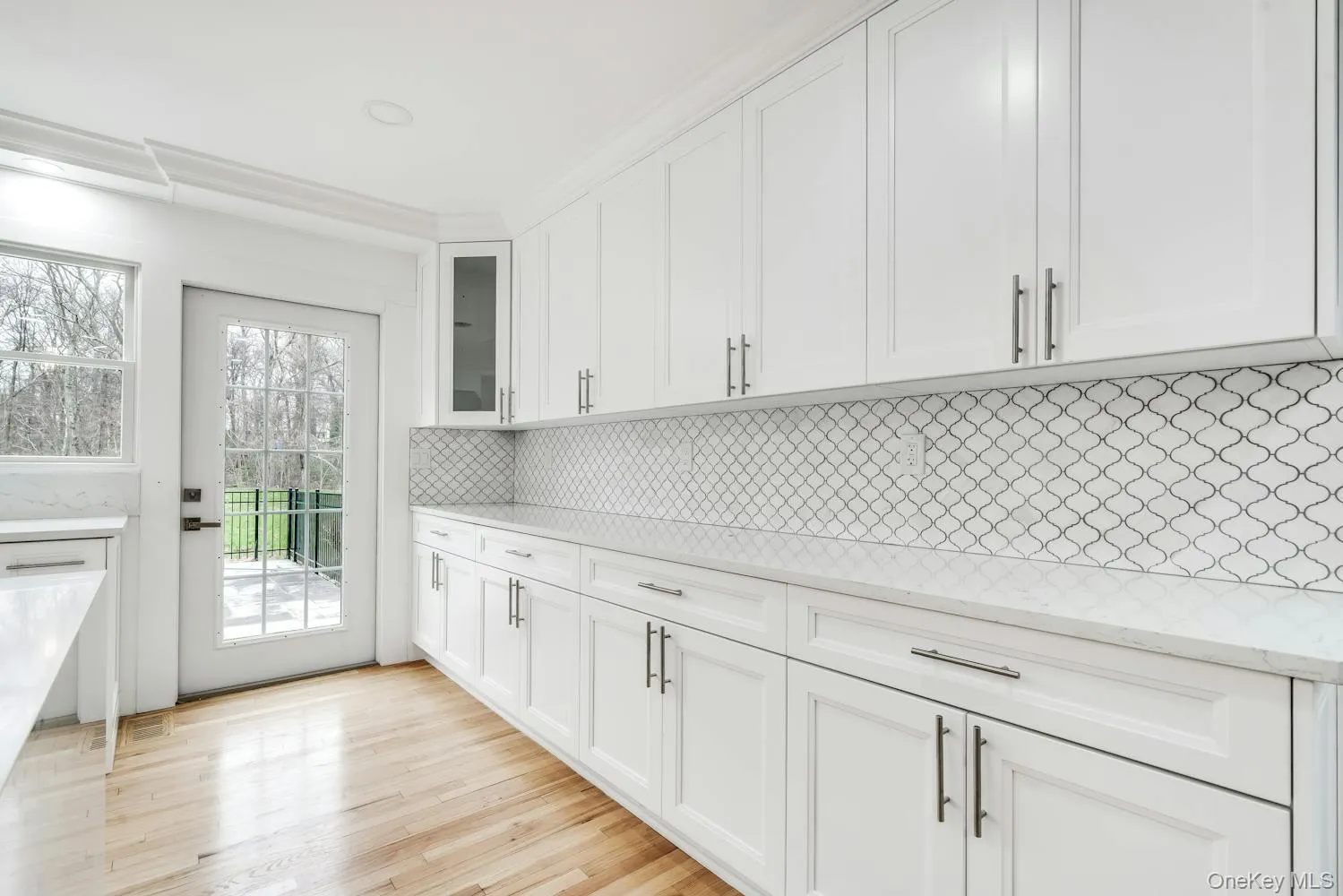 Kitchen featuring white cabinets, light stone countertops, light wood finished floors, decorative backsplash, and glass insert cabinets Kitchen featuring white cabinets, light stone countertops, light wood finished floors, decorative backsplash, and glass insert cabinets