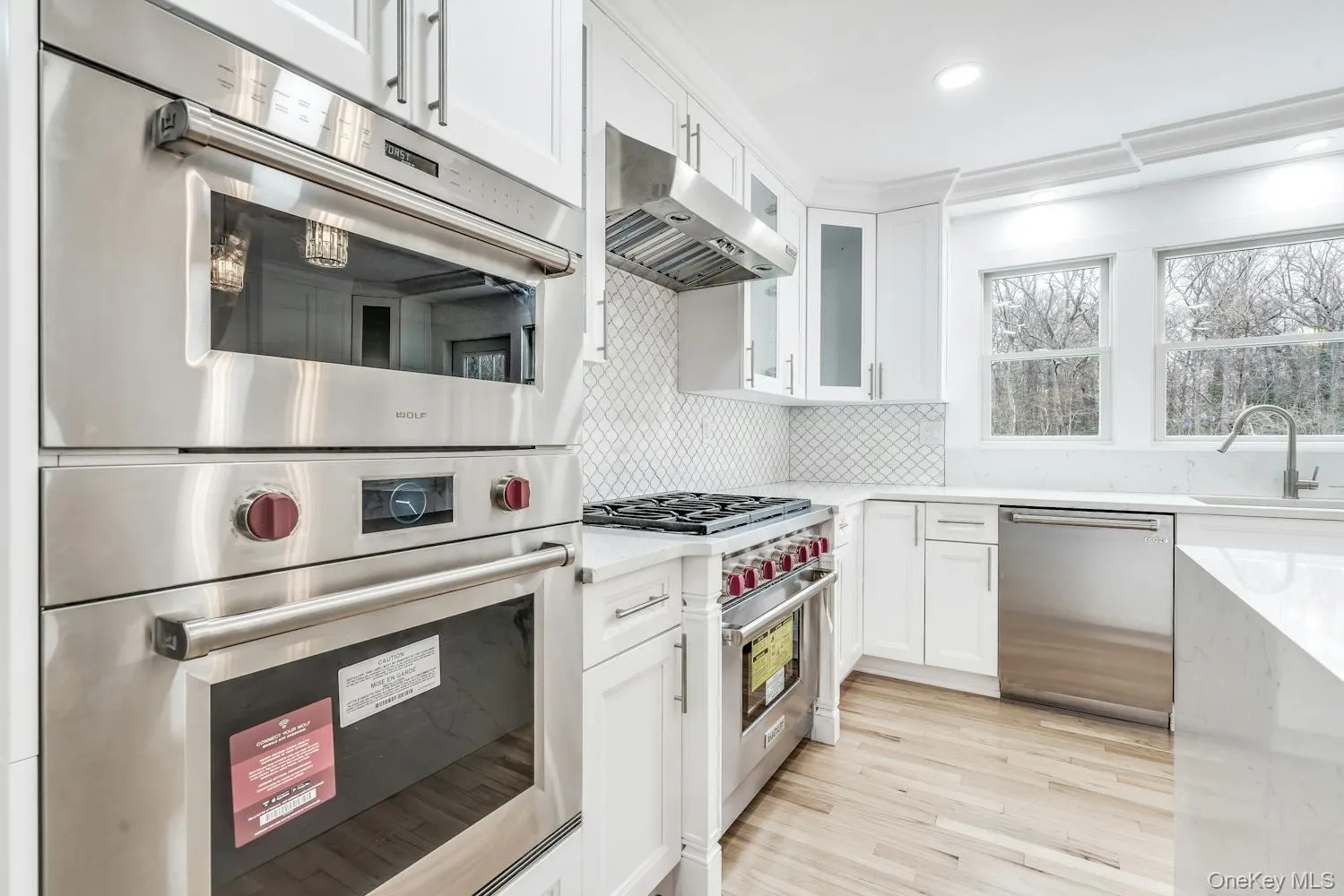 Kitchen with a sink, ventilation hood, white cabinetry, and stainless steel appliances Kitchen with a sink, ventilation hood, white cabinetry, and stainless steel appliances
