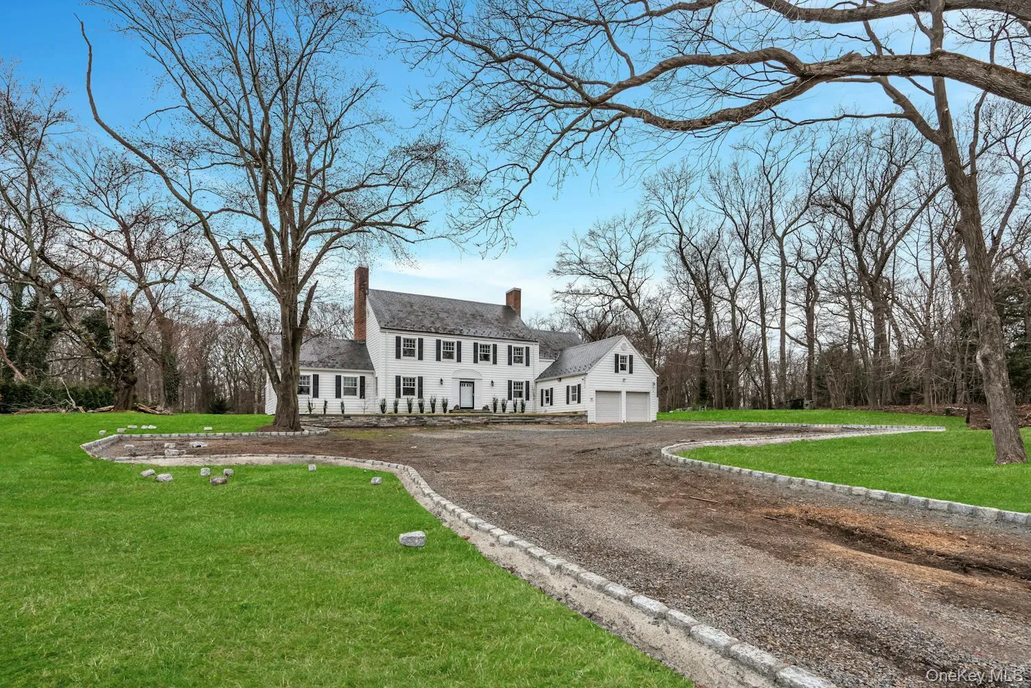 Colonial-style house featuring a garage, a chimney, a front lawn, and dirt driveway Colonial-style house featuring a garage, a chimney, a front lawn, and dirt driveway