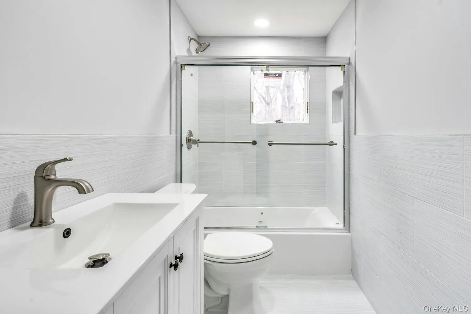 Bathroom featuring vanity, combined bath / shower with glass door, toilet, and tile walls Bathroom featuring vanity, combined bath / shower with glass door, toilet, and tile walls