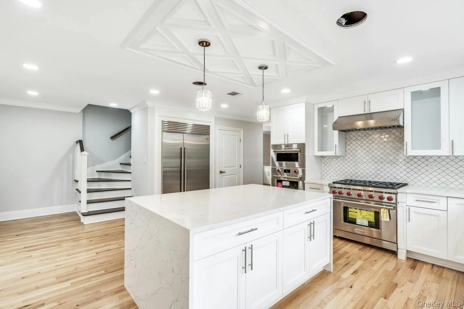 Kitchen featuring decorative backsplash, high end appliances, light wood-type flooring, under cabinet range hood, and white cabinets Kitchen featuring decorative backsplash, high end appliances, light wood-type flooring, under cabinet range hood, and white cabinets