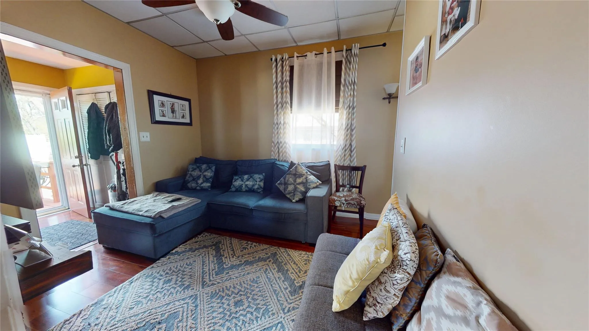 Living area with a healthy amount of sunlight, a paneled ceiling, and a ceiling fan Living area with a healthy amount of sunlight, a paneled ceiling, and a ceiling fan