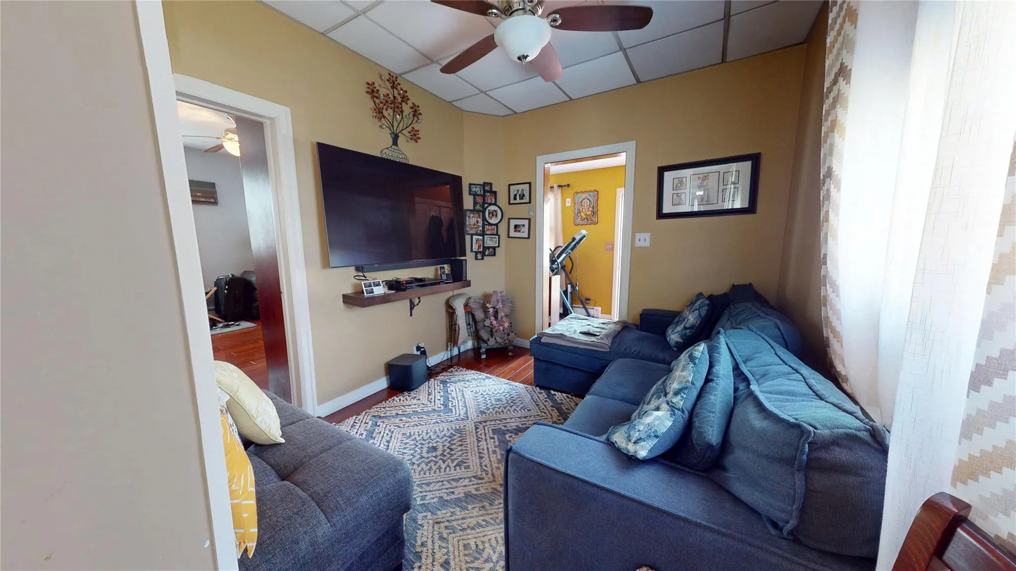 Living area with wood finished floors, a drop ceiling, a ceiling fan, and baseboards Living area with wood finished floors, a drop ceiling, a ceiling fan, and baseboards
