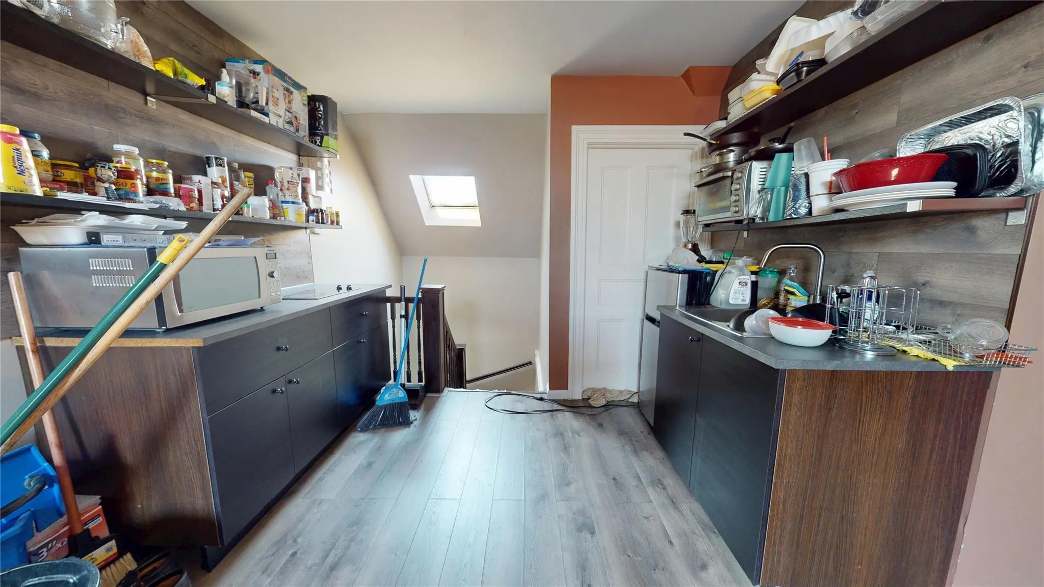 Kitchen featuring dark countertops, light wood-style floors, open shelves, and a skylight Kitchen featuring dark countertops, light wood-style floors, open shelves, and a skylight