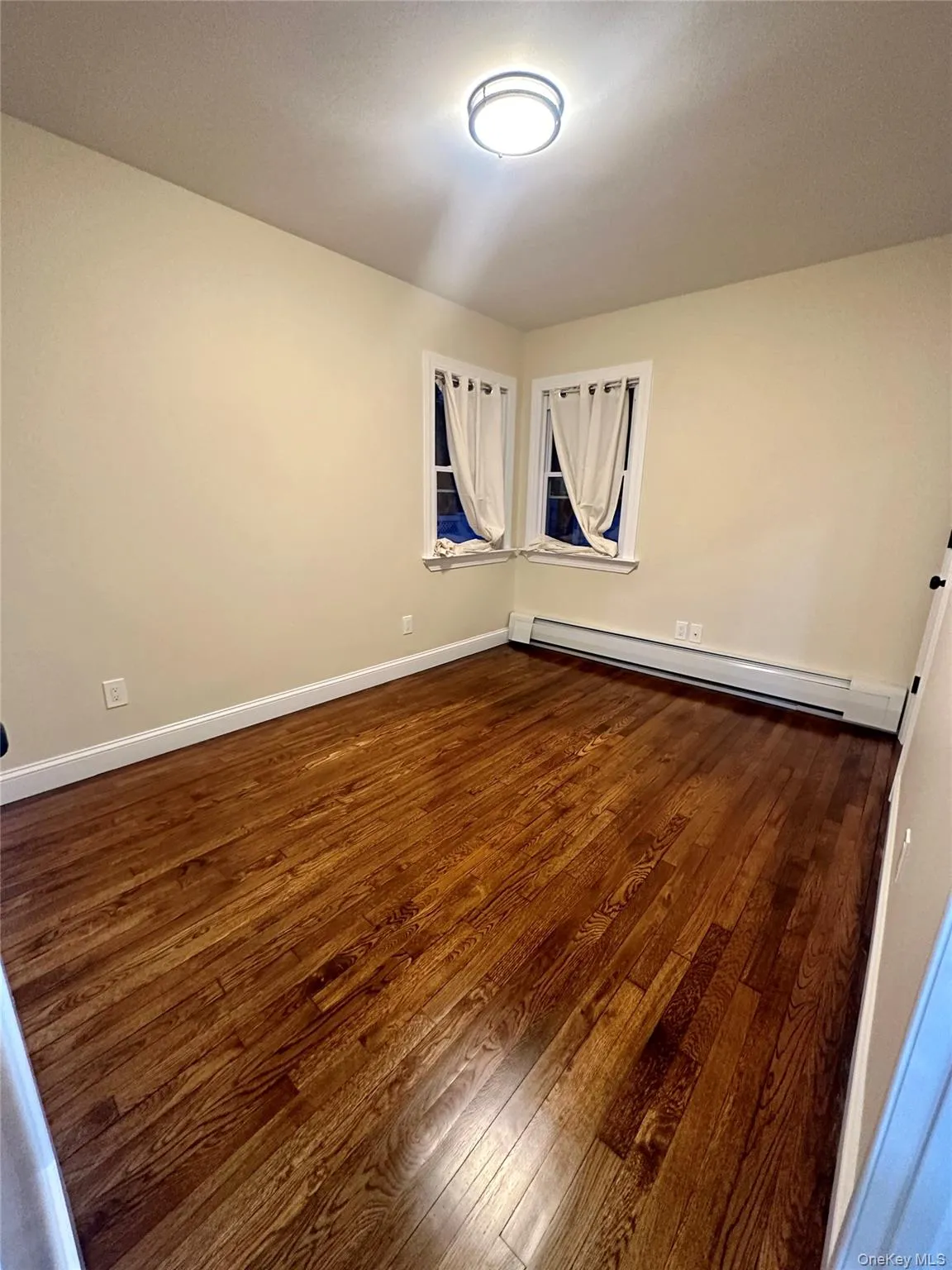 Spare room featuring dark wood-style floors, baseboards, and a baseboard heating unit Spare room featuring dark wood-style floors, baseboards, and a baseboard heating unit