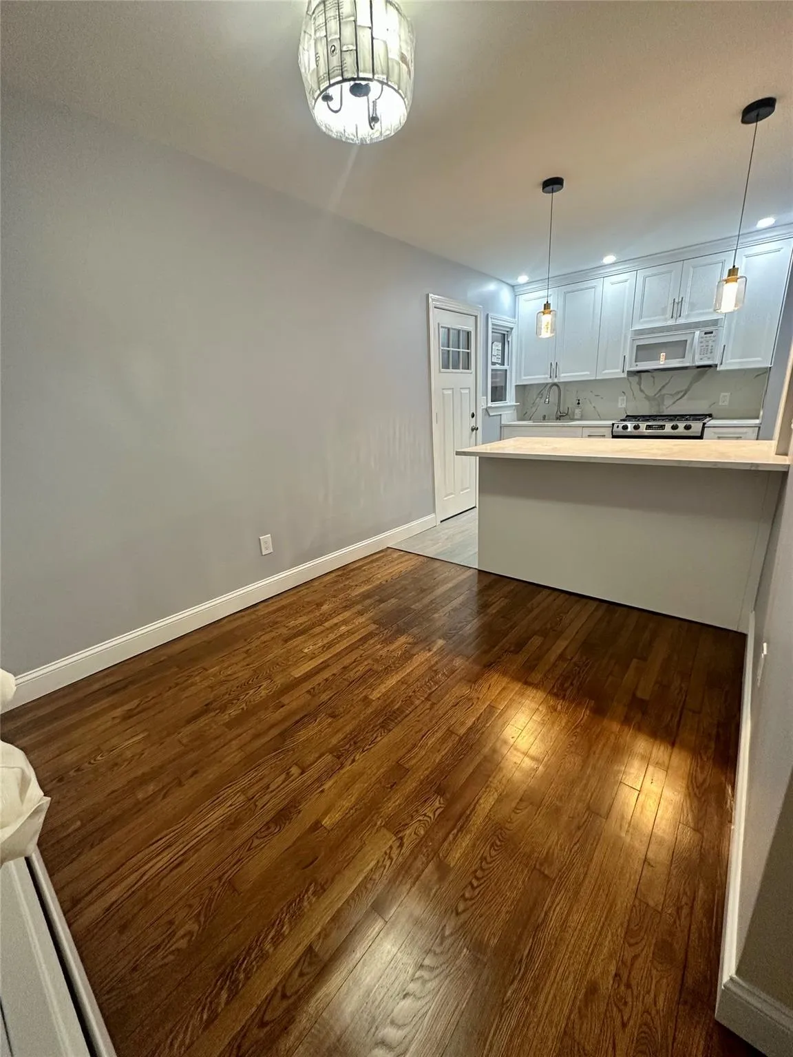 Kitchen with white microwave, pendant lighting, light countertops, dark wood-style floors, and stainless steel gas range Kitchen with white microwave, pendant lighting, light countertops, dark wood-style floors, and stainless steel gas range