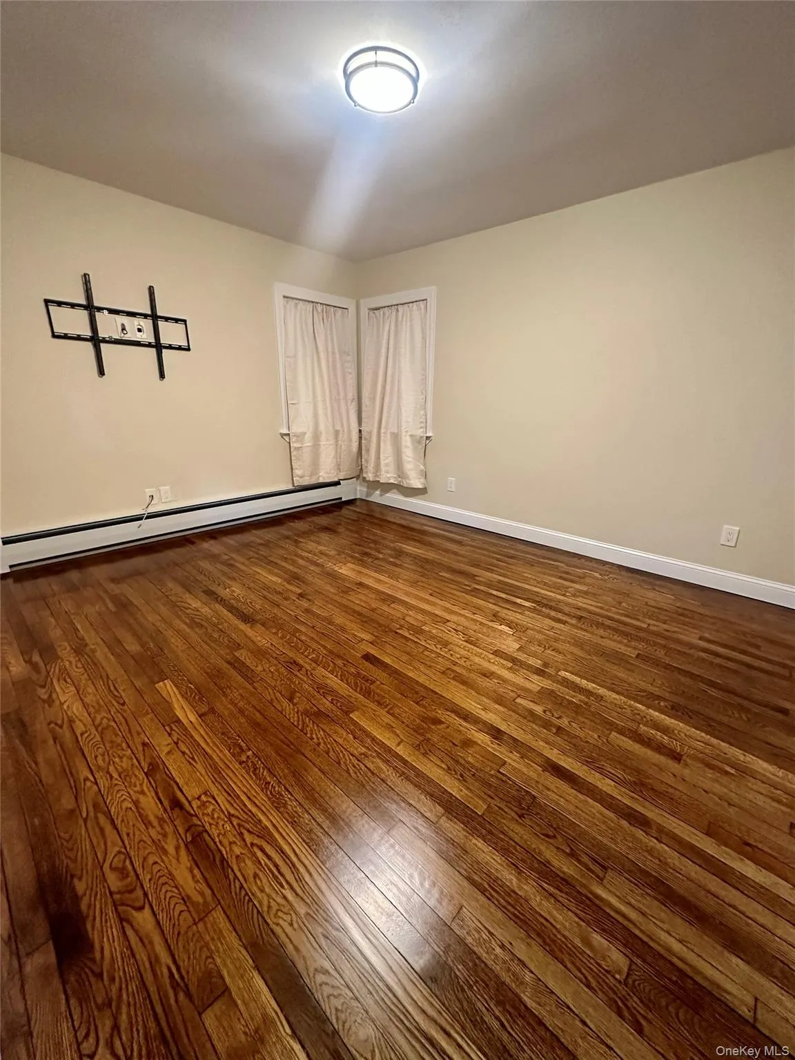 Spare room featuring dark wood-style floors, baseboard heating, and baseboards Spare room featuring dark wood-style floors, baseboard heating, and baseboards