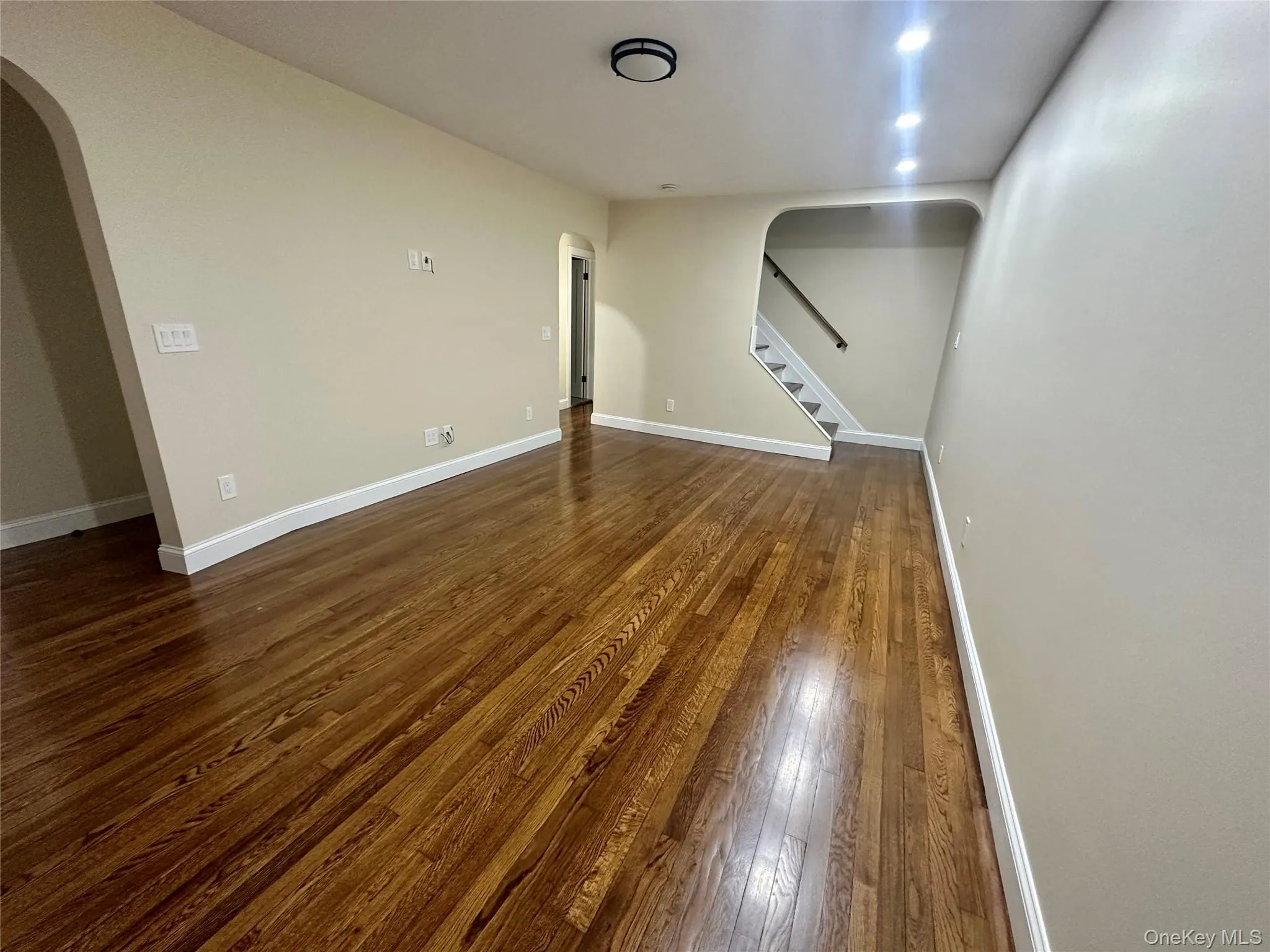 Unfurnished living room featuring baseboards, arched walkways, stairs, and dark wood-style flooring Unfurnished living room featuring baseboards, arched walkways, stairs, and dark wood-style flooring