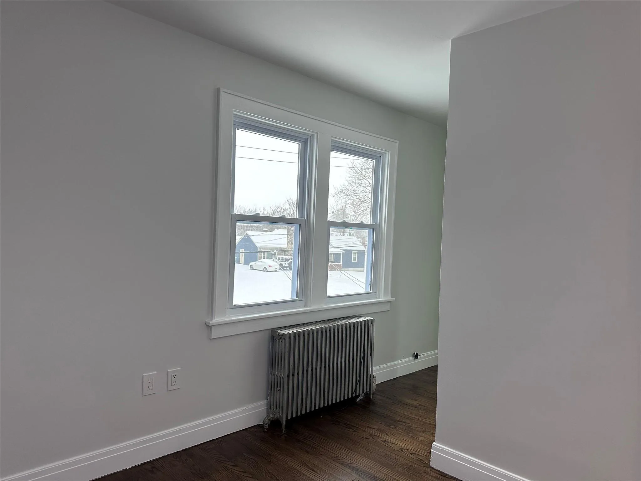Unfurnished room with radiator heating unit, dark wood finished floors, and baseboards Unfurnished room with radiator heating unit, dark wood finished floors, and baseboards