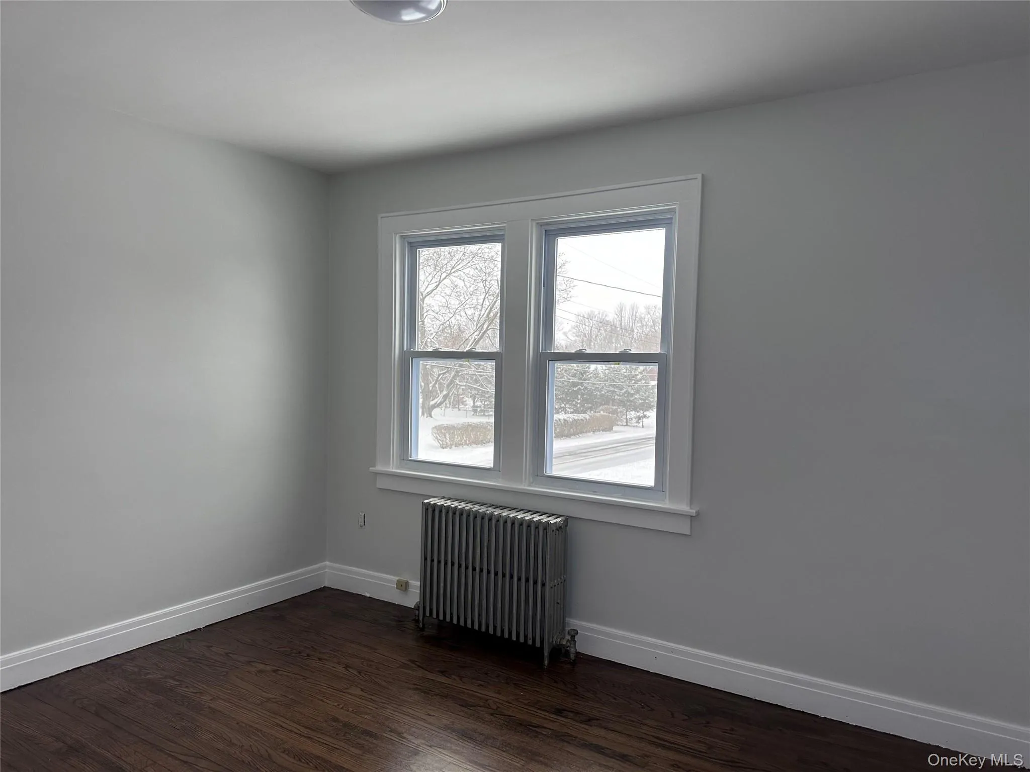 Empty room featuring radiator heating unit, dark wood finished floors, and baseboards Empty room featuring radiator heating unit, dark wood finished floors, and baseboards