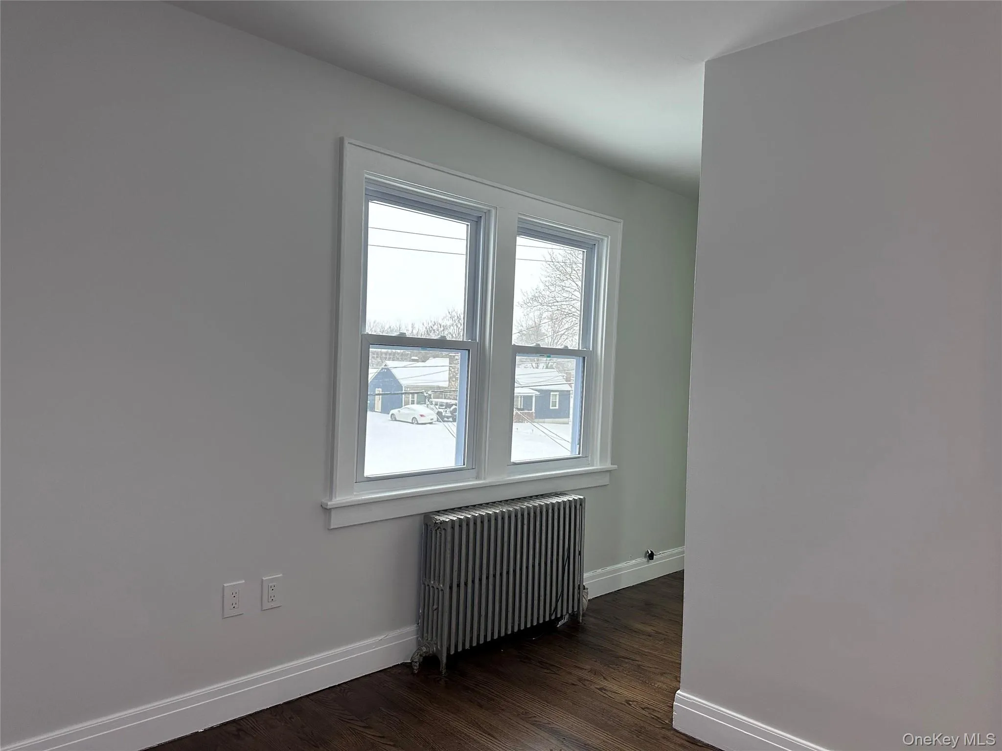 Unfurnished room with radiator heating unit, dark wood finished floors, and baseboards Unfurnished room with radiator heating unit, dark wood finished floors, and baseboards
