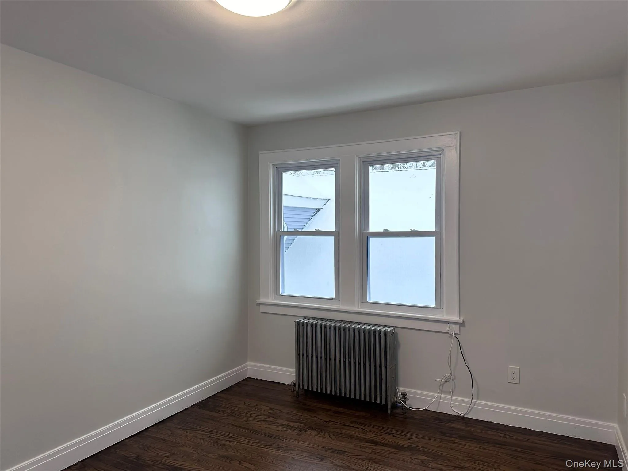 Empty room with baseboards, radiator, and dark wood finished floors Empty room with baseboards, radiator, and dark wood finished floors