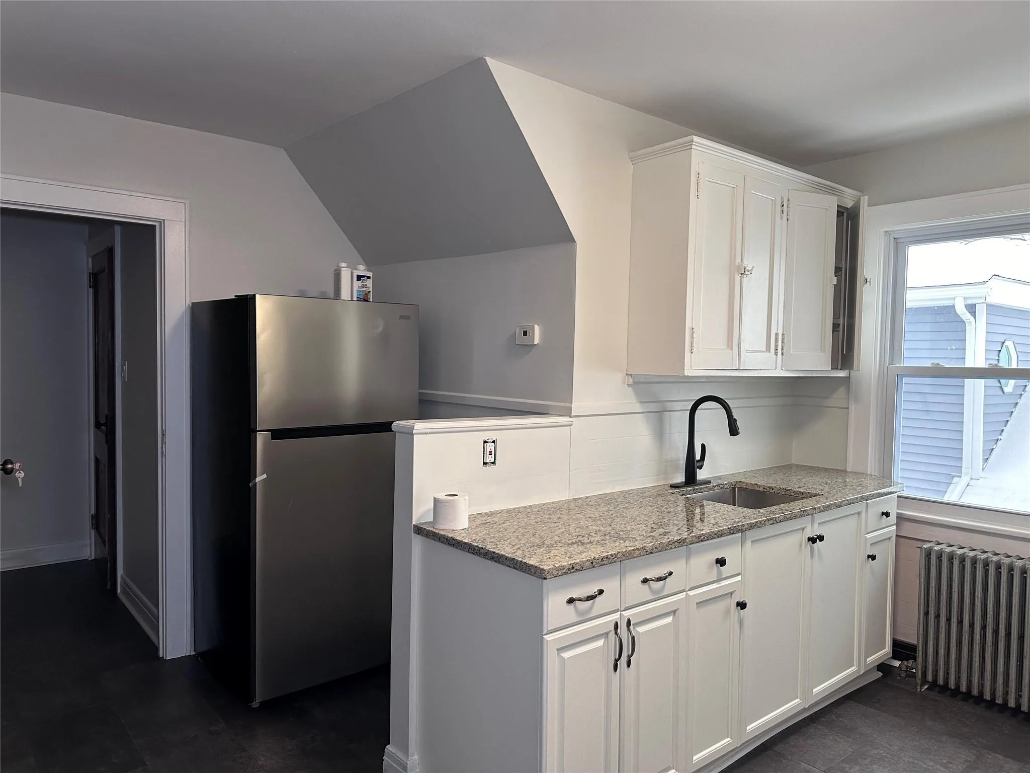 Kitchen featuring a sink, white cabinets, freestanding refrigerator, and radiator Kitchen featuring a sink, white cabinets, freestanding refrigerator, and radiator