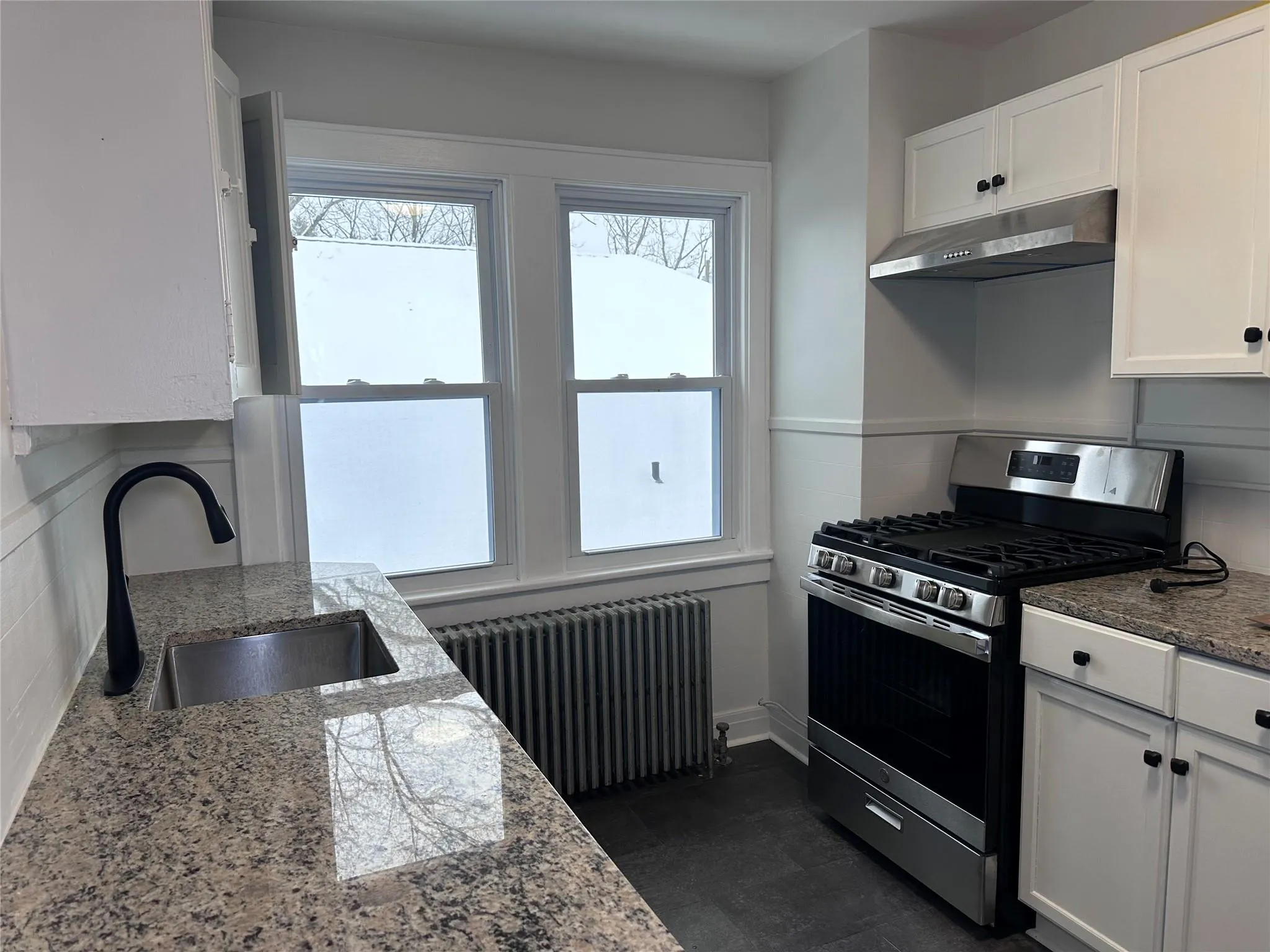 Kitchen with stainless steel gas stove, under cabinet range hood, white cabinets, radiator heating unit, and a sink Kitchen with stainless steel gas stove, under cabinet range hood, white cabinets, radiator heating unit, and a sink