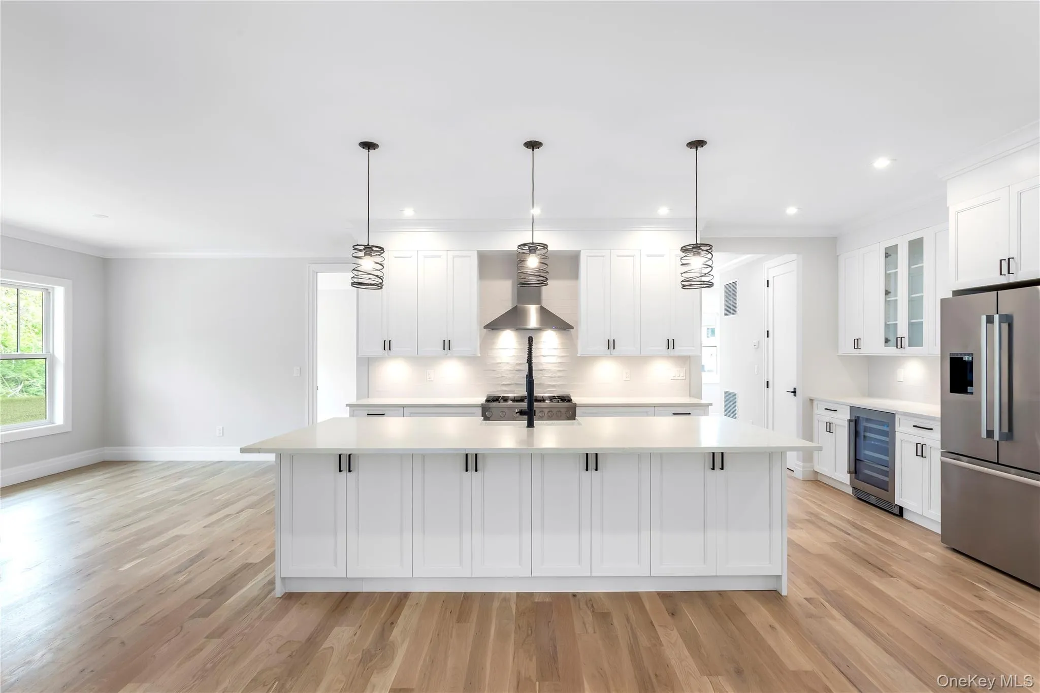 Kitchen featuring stainless steel fridge with ice dispenser, beverage cooler, light countertops, light wood finished floors, and ornamental molding Kitchen featuring stainless steel fridge with ice dispenser, beverage cooler, light countertops, light wood finished floors, and ornamental molding